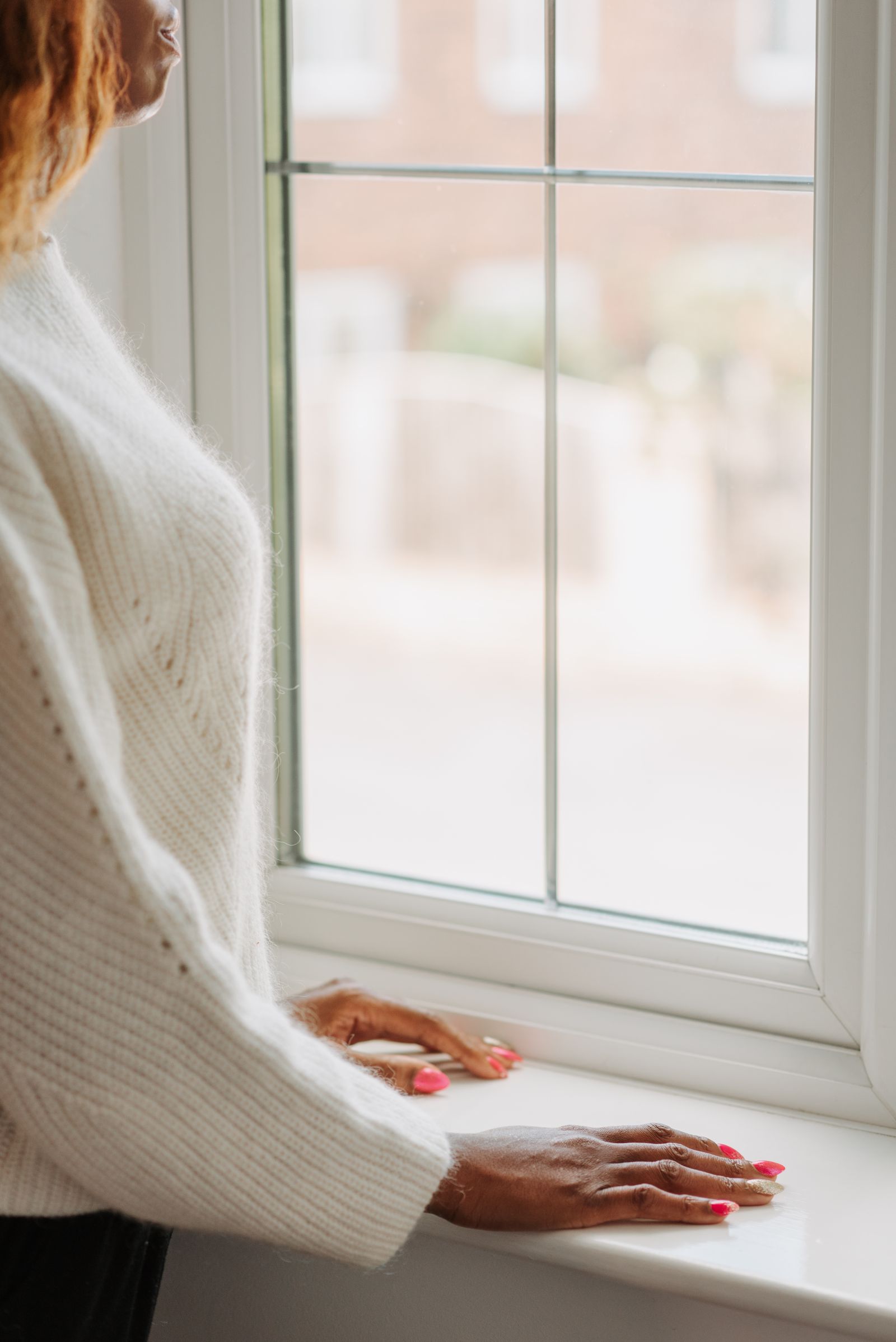 Woman standing at a window with her hands on the sill, thinking about divorce and afraid of who her spouse will become