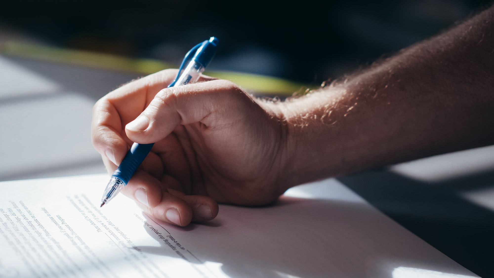 A hand holding a pen over divorce settlement papers, pausing before signing