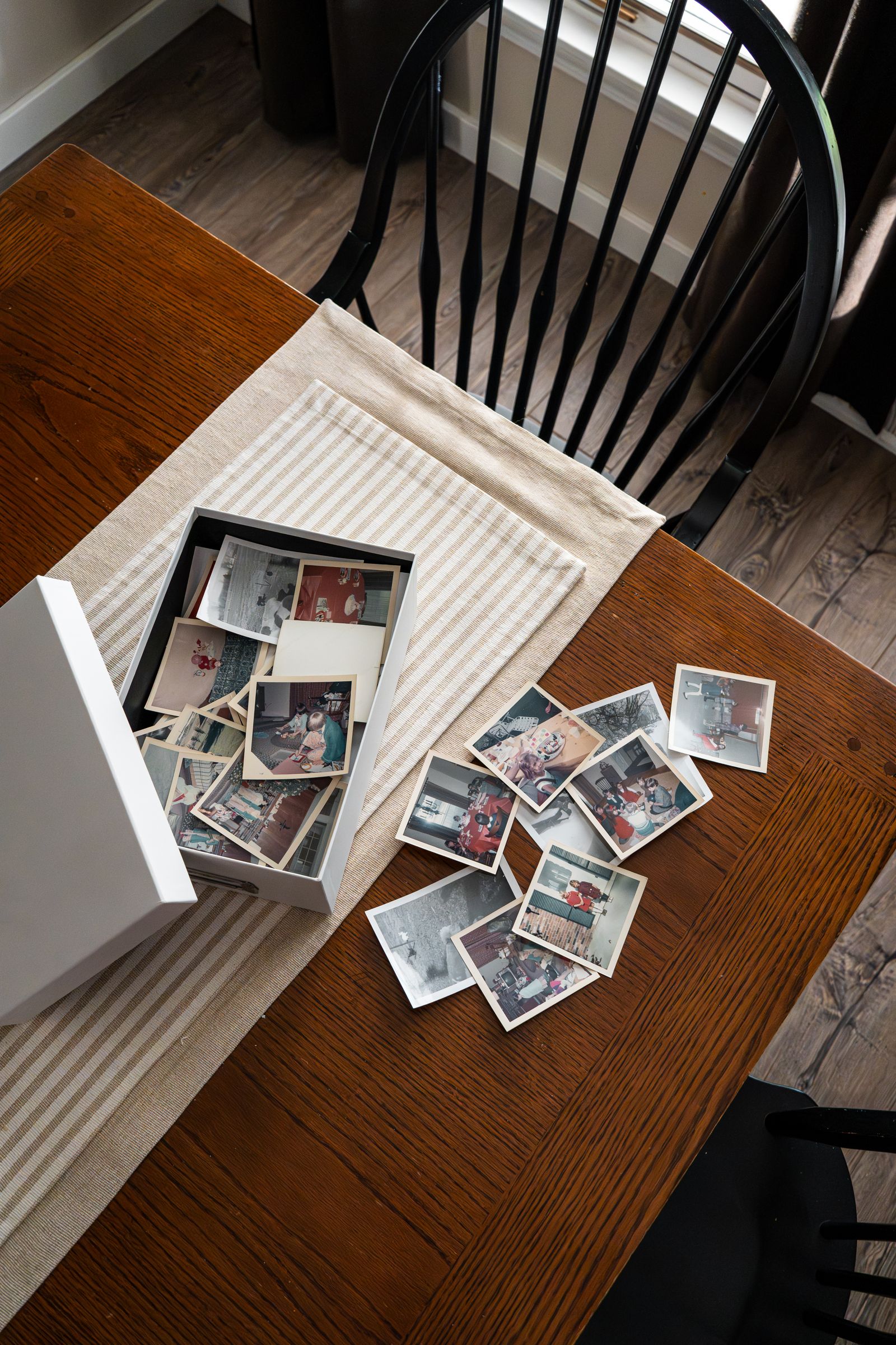 A box of old family snapshots spread across a wooden kitchen table
